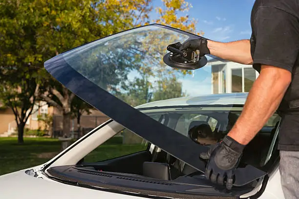 Technician using a suction tool to lift and align a new windshield during a mobile windshield replacement.